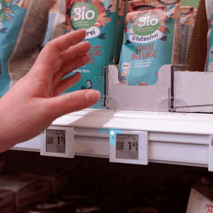 Eine Hand greift nach einem dm-Produkt im Regal, an welchem das elektronische Preisetikett (ESL) weiß-bläulich aufblinkt
